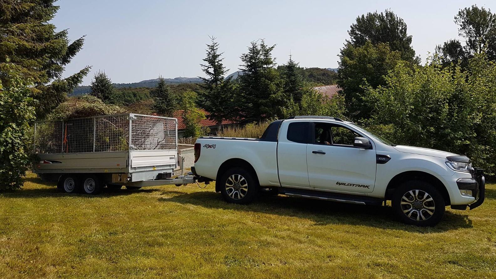 Arbeidsbil med henger parkert på plen